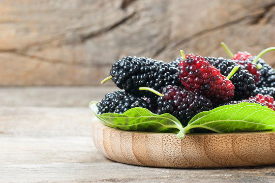 Fresh ripe black mulberry berry fruit with leaf on rustic wooden background, blackberry summer red fruits concept 