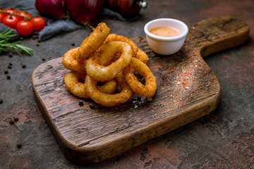 Onion rings in batter with sause on old board and dark rustic concrete background