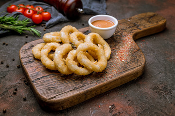 Rings of squid in batter with sauce on the board on dark concrete rustic background