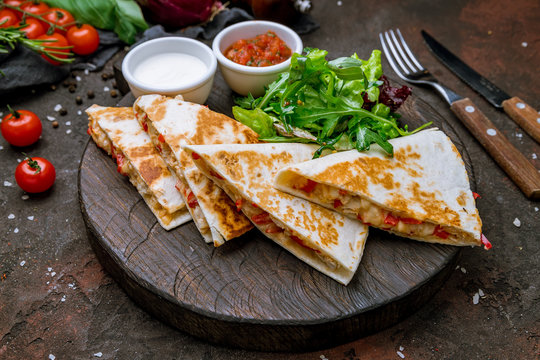 Quesadilla with chicken and sauces on dark board , on dark rustic concrete background