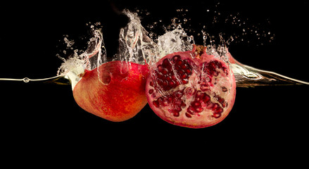 Pomegranate splashing into water against black background.