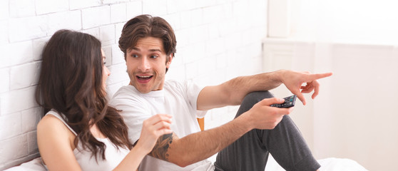 Emotional millennial couple watching tv at home