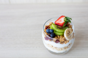 Healthy breakfast ,bowl of oat with yogurt, kiwi, raspberries, blueberries, strawberries, banana on white wooden.