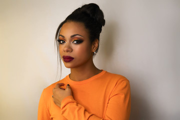 Portrait of attractive afro american young woman with fashion luxury makeup orange-coloured shades and her hair scraped back into high bun. Perfect Skin. Long eyelashes. Pouty lips. Beauty industry. - obrazy, fototapety, plakaty