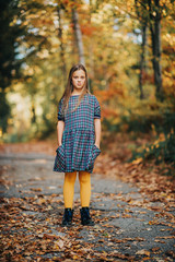 Autumn portrait of pretty young girl, kid model posing outdoor in forest, wearing plaid dress and yellow tights