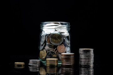 growth graph from stack of coin and clear jar with thai baht coin on black background. concept for financial and saving money