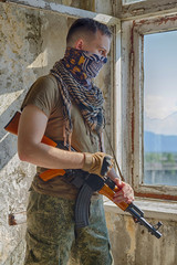 Man in military camo clothes, half face bandit mask and shemagh scarf with machine gun in hands...