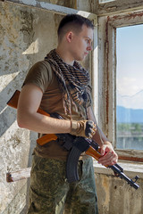 Man in military camo clothes and shemagh scarf with machine gun in hands staying inside abandoned...