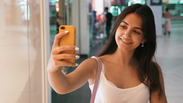 Portrait of young cheerful caucasian woman doing sefie in the mall