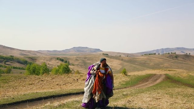 man beard mustache striped white-yellow T-shirt green hat jeans with red backpack collects carries off purple gray parachute against the background mountains, caucasian
