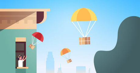 woman in window catching parcel box falling down with parachute from sky transportation shipping package air mail express delivery concept modern house building exterior portrait horizontal
