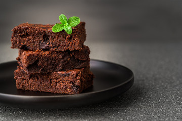 Dark chocolate and cocoa brownie fudge cakes dessert with mint against black and grey stone background
