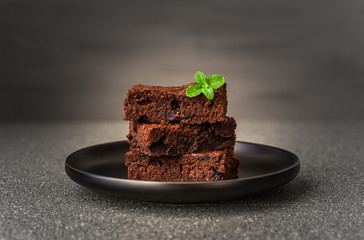 Dark chocolate and cocoa brownie fudge cakes dessert with mint against black and grey stone background