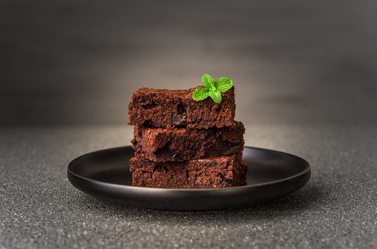 Dark chocolate and cocoa brownie fudge cakes dessert with mint against black and grey stone background