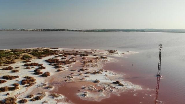 A panoramic aerial view high above the salt lake of Torrevieja in Spain. The lagoon is dyed red. In the background the salt mountains, the city and the deep blue Mediterranean sea.