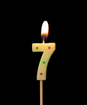Burning birthday candle isolated on black background, number 7