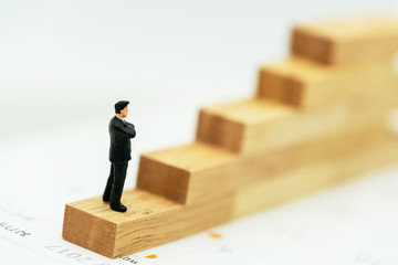 Miniature people: Business man standing on a wooden box.
