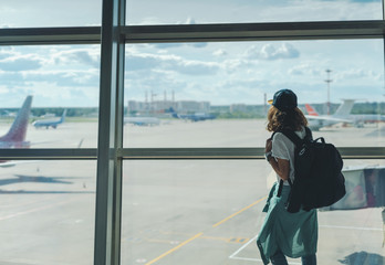 happy young girl traveler with backpack at the airport on the background of the takeoff field