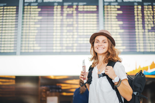 Happy Young Girl Traveler At The Airport On The Background Of The Departures Board