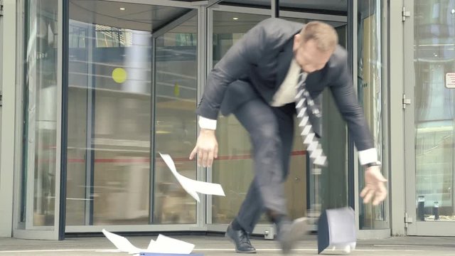 Business man with papers and notebook coming out of the office building hurrying and stumbling