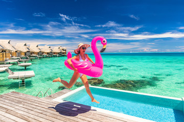 Vacation fun woman in bikini with funny inflatable pink flamingo pool float running of joy jumping...