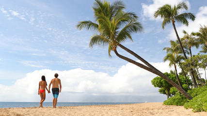 Beach summer vacation couple walking under palm trees in bikini and swim trunks.