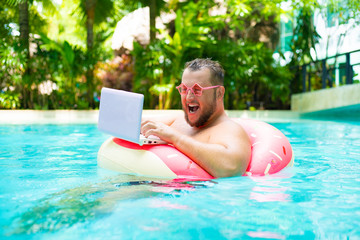 screaming Funny fat male in pink glasses on an inflatable circle in the pool works on a laptop...