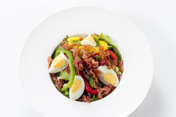 Fresh Caesar Salad with Deep-fried Bacon and Boiled Eggs on White Porcelain Circle Plate, Isolated on White Background with Shadow. Close-Up Top View, Selective Focus at Food.