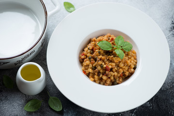 Italian fregola pasta served in a white plate with fresh green basil and olive oil, studio shot