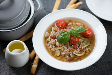 Italian spelt and vegetable soup served in a white plate, horizontal shot over grey stone background
