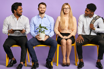 young people of different nationalities sitting in a row in friendly atmosphere isolated on purple waiting for job interview