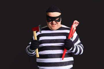 cheerful happy thief with a pipe wrench and ax in his hands looking at the camera with cunning...