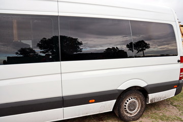 Close-up view of a minibus and cars standing on the shore of a lake. The reflection in the windows...