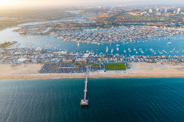 Aerial view from above over Newport Beach in coastal Orange County, California on a sunny day from above with the ocean, pier and harbor in view.