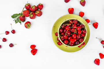 Top view of bowl of fresh sweet cherries with cherries on a white wooden background with space for text