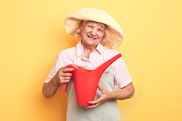 beautiful happy girl in grey apron and yellow hat holding watering can, isolated on yellow background. close up photo.gardern concept. lifestyle, free time, spare time, studio shot