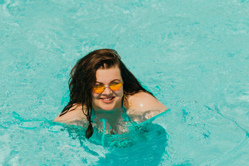 Attractive busty curvy woman in a blue swimsuit and yellow sunglasses resting and swims in the...