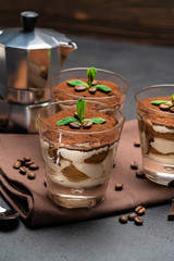 Classic tiramisu dessert in a glass and coffee maker on dark concrete background