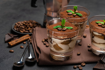 Classic tiramisu dessert in a glass and coffee maker on dark concrete background