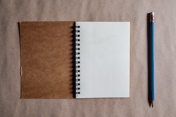 Blue pencil with brown note book on brown paper background