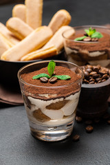 Classic tiramisu dessert in a glass and savoiardi cookies on dark concrete background