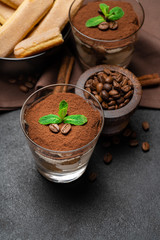 Classic tiramisu dessert in a glass and savoiardi cookies on dark concrete background