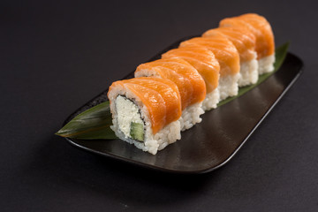 Close up sushi rolls in a black plate on dark background