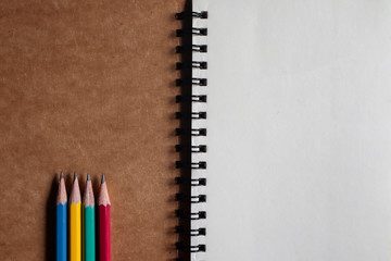 Multi-colored pencils with brown note book on brown paper background