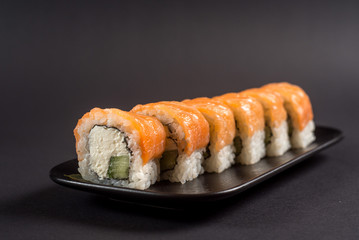 Close up sushi rolls in a black plate on dark background