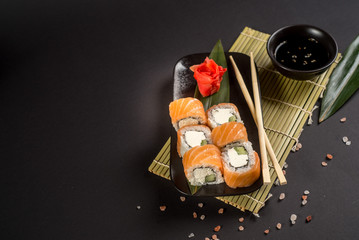 Close up sushi rolls in a black plate on dark background