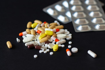 Multicolored different pills with two grey shine blisters on the black background. Treatment of viruses, sickness, excess weight, depression, insomnia, diseases of the stomach and heart. 