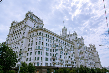 Residential building on the waterfront in Ar Deco style. Light beige color facade and spire on the roof. There are massive wooden doors and fretworks.