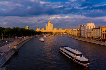 the ship sails on the river in the sunset light. a cityscape and a residential building with a spire on the background. Landscape of Moscow river