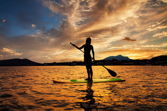 Stand up paddle boarding on a quiet sea with warm summer sunset colors.
